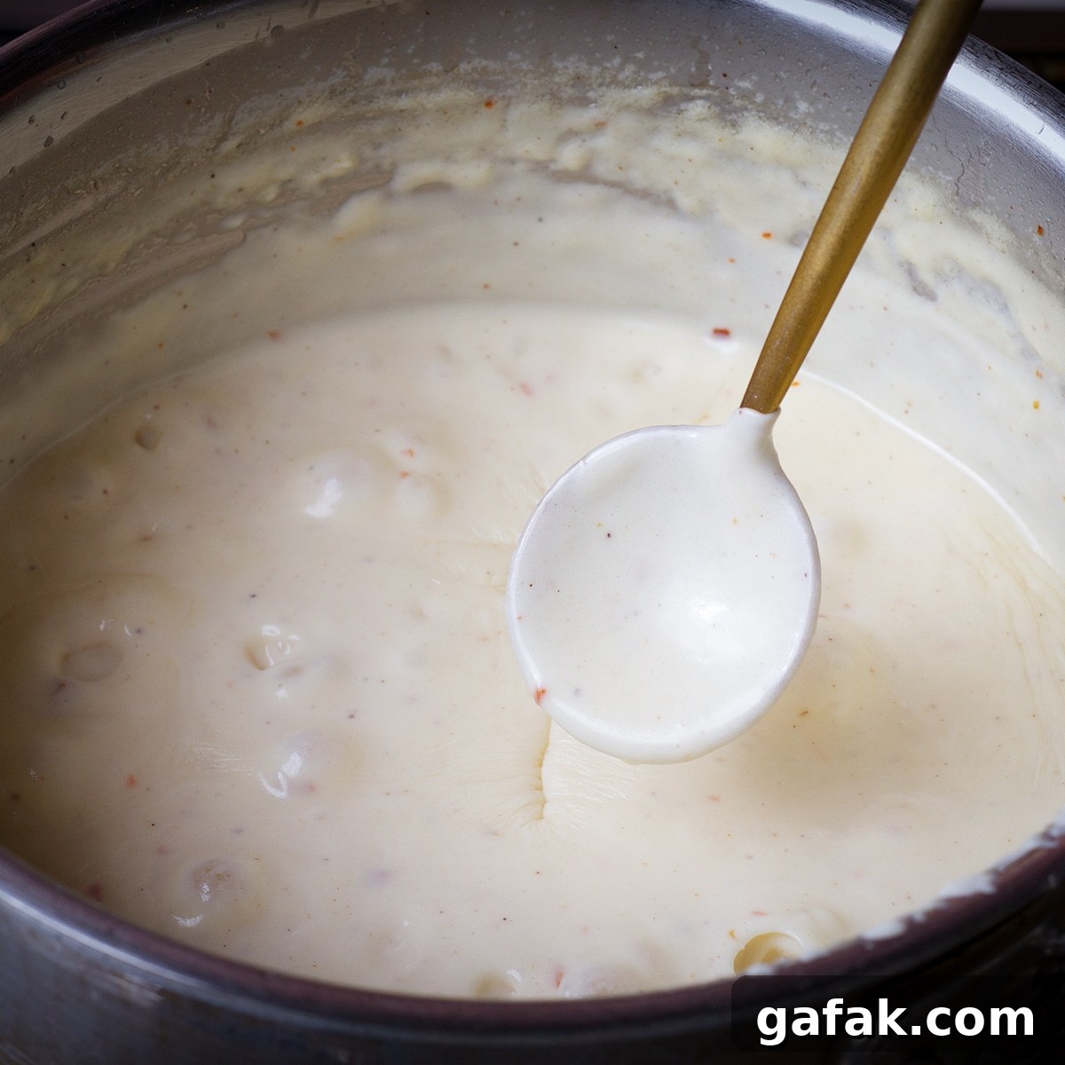 Creamy Mushroom Lasagna with Parmesan Béchamel Sauce 8 Lifting a spoon out of a saucepan of béchamel sauce to test how thick the sauce is.