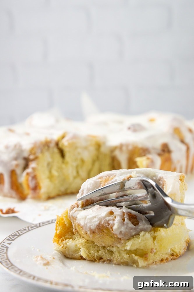 A soft cinnamon roll on a white plate with a fork pressing into it