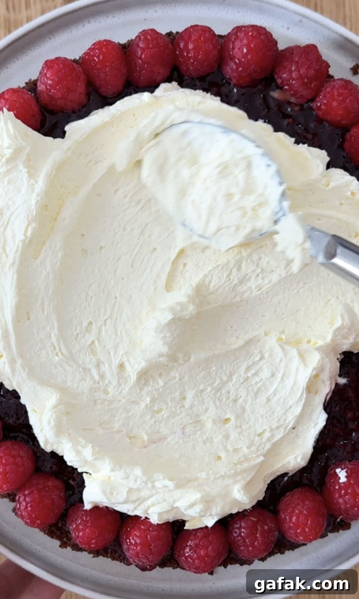 adding whipped cream to the chocolate raspberry cake.