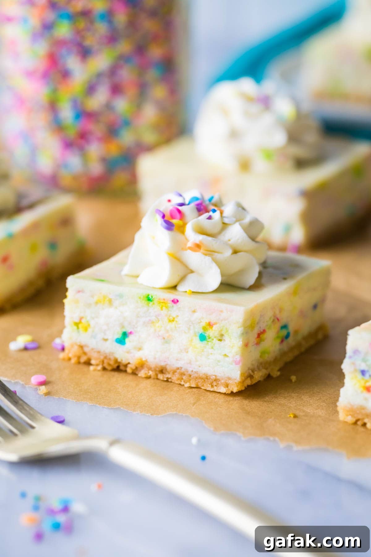 funfetti cheesecake bar topped with whipped cream and sprinkles on brown parchment