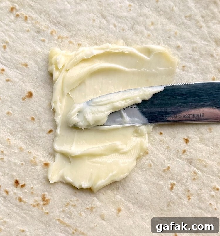 Soft butter being spread onto a tortilla with a butter knife.