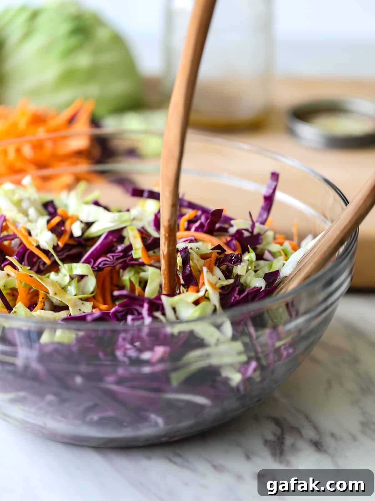 Coleslaw in a clear bowl with wood serving tongs.