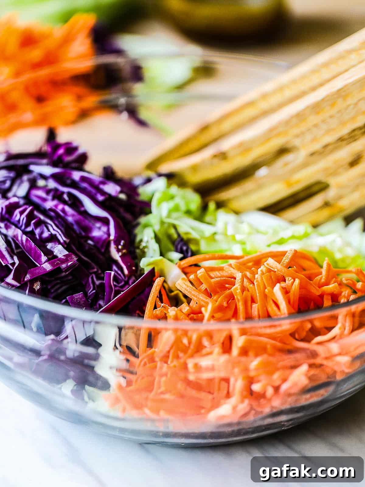 Shredded carrots and cabbages in a clear bowl ready to be tossed.