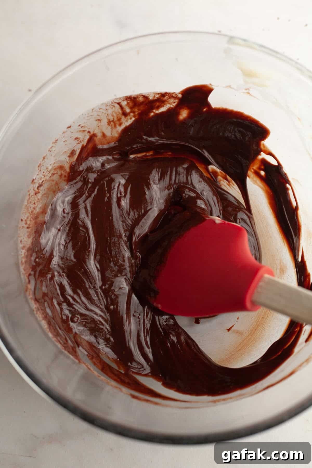 Chocolate ganache in a glass bowl with a red rubber spatula.